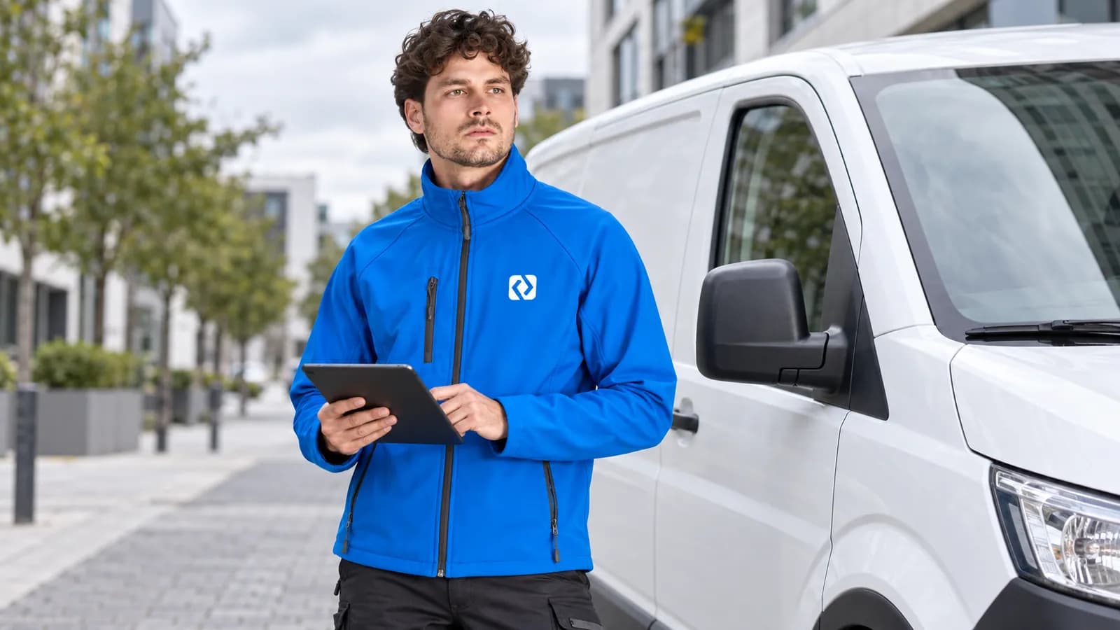 Serwisant w niebieskiej kurtce softshell z logo na piersi przy samochodzie dostawczym
